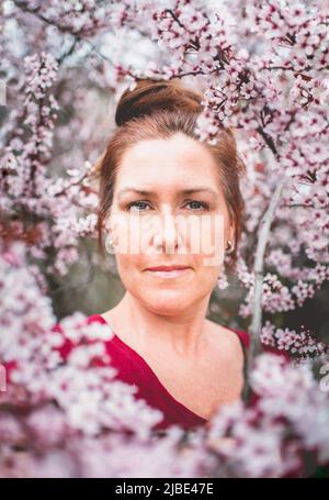 Close up portrait of woman among branches of flowering tree in spring. Stock Photo