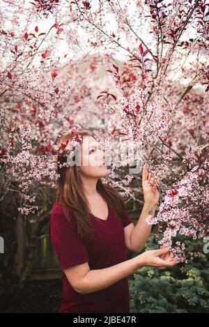 Pretty woman standing among branches of flowering tree in spring. Stock Photo