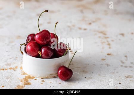 Fresh cherries close up in white ceramic bowl on textured background, copy space Stock Photo