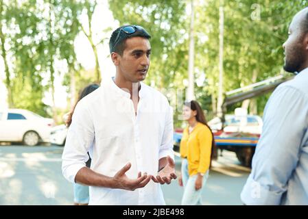 Happy two multiracial male best friends talking while standing in the street, african guy talking to afghan buddy at outdoor meeting. Smiling multieth Stock Photo