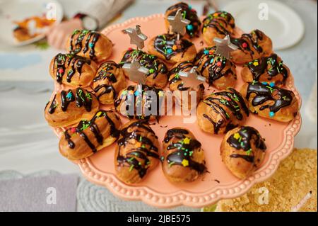 custard cakes with chocolate fondant on a tray on a festive table with treats and drinks Stock Photo