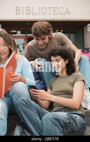 Happy young diverse friends sharing smartphone in campus Stock Photo