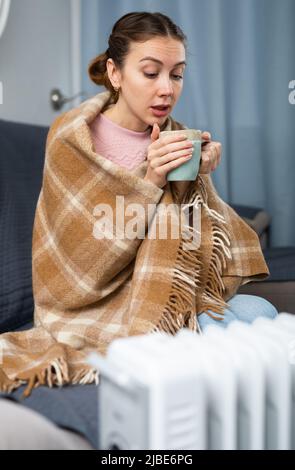 Adult woman with cup near heater in home closeup Stock Photo