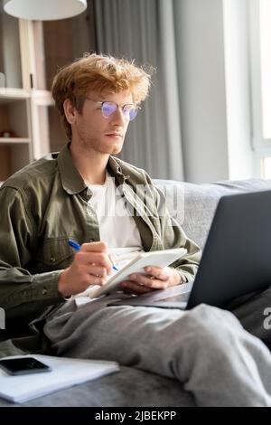 Focused young ginger man watching webinar using laptop to study online Stock Photo
