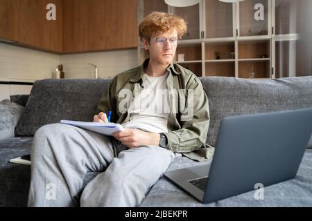 Focused young ginger irish man watching webinar video course writing notes Stock Photo