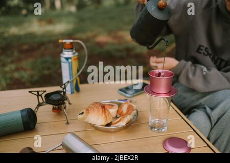 Coffee drip while camping in forest with sunshine. Coffee maker outdoor, campsite morning picnic lifestyle, person cooking hot drink in nature camping Stock Photo