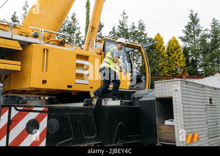 Operator climbing on Construction crane lifting heavy freight. Modern mobile transportation technologies help building house. Real estate professional Stock Photo