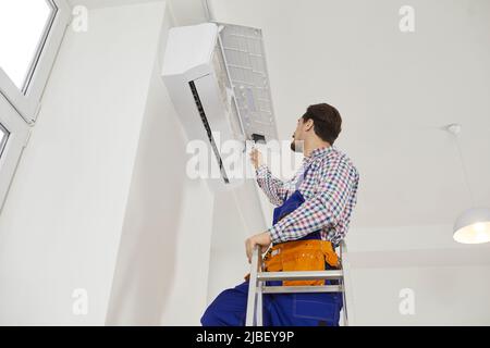 Male installation service worker repairs, cleans and maintains air conditioner that hangs on wall. Stock Photo