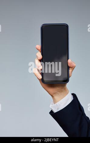 Close up of female hand holding smartphone with blank screen to camera against grey background Stock Photo
