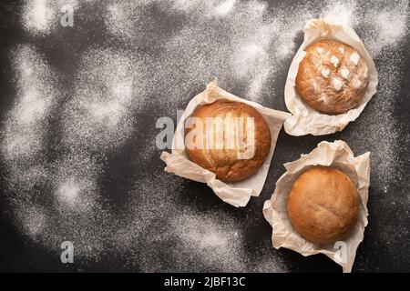 Fresh bakery food, rustic crispy loaves of bread and buns on black stone background with flour, homemade baking, top view, flat lay Stock Photo