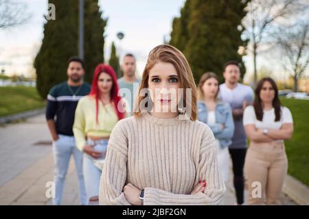 Confident woman looking at camera and smiling while standing with crossed arms in front of group of people. Friendship, union and team concept. Stock Photo