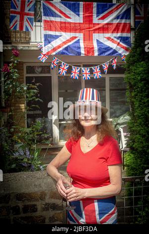 Woman in front of Union Jack flags and bunting outside a council house in London to celebrate 70 years of Her Majesty the Queen's reign. Stock Photo