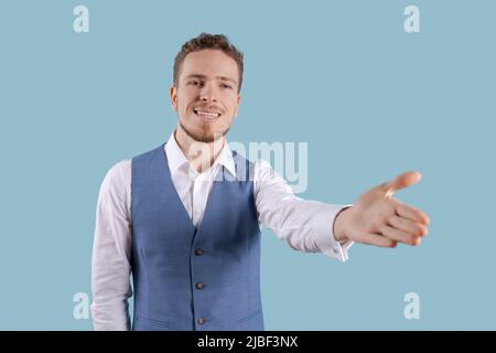 Portrait handsome business man with charming smile, gesturing with his hands while standing at casual post as if talking on a blue background. Caucasian guy leads successful negotiations Stock Photo