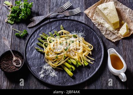 roasted asparagus spears with spaghetti sprinkled with shredded pecorino cheese and parsley on black plate on dark wood table, horizontal view from ab Stock Photo