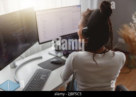 Back view of young professional woman programmer working from home sitting at desk Stock Photo