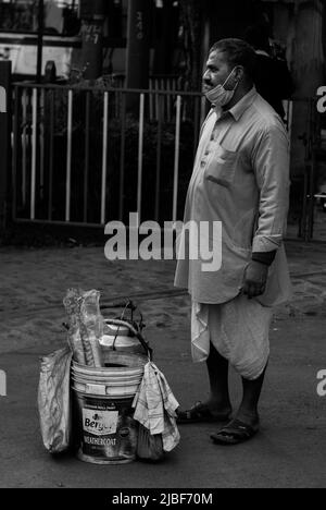Kolkata, India - January 2, 2022: A tea seller wearing traditional indian dhoti, standing and waiting for customers. A bucket containing tea kettle an Stock Photo