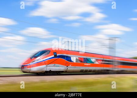 A Frecciarossa (ETR 1000) high speed train from italian rail company Trenitalia is driving at full speed in the countryside.