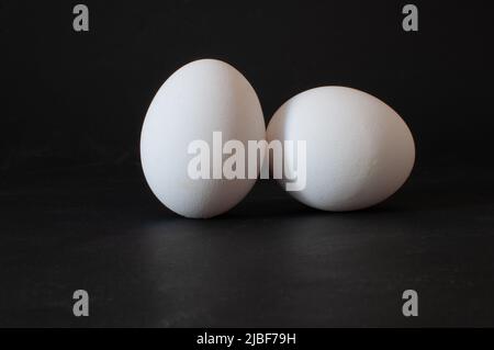 Two eggs, profile view of white raw chicken eggs isolated on dark background, selective focus. Stock Photo