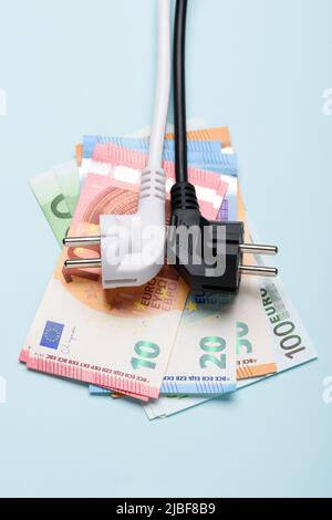 Electric power plugs on Euro banknotes on blue background. Concept of expensive electricity costs and rise in energy bill prices. Stock Photo