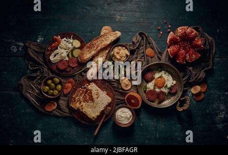 From above of arrangement of assorted dishes including fried eggs with sausage and honey served on napkin on wooden table for Turkish breakfast Stock Photo