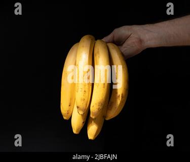 Banana bunch in male hand on black background Stock Photo
