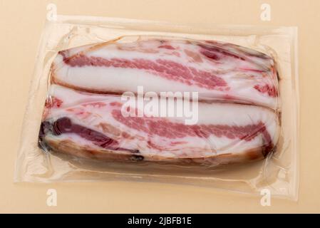 Italian Guanciale, slices dry cured pork cheek in in vacuum packed sealed for sous vide cooking isolated on light brown background Stock Photo
