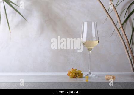 A glass of white wine, a cork and a bunch of grapes on a stone table. Light background. Stock Photo