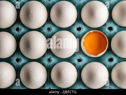 Organic fresh chicken eggs arranged in egg tray. half broken egg with yolk visible Stock Photo