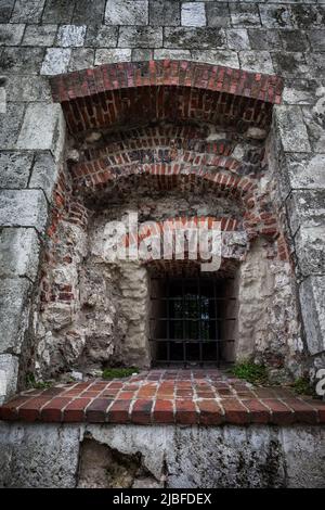 Barred recessed window in medieval castle, old stone structure with brick elements in arches and windowsill. Stock Photo