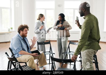 Two young interracial men greeting each other by waving hands before psychological session in front of female counselor and black woman Stock Photo