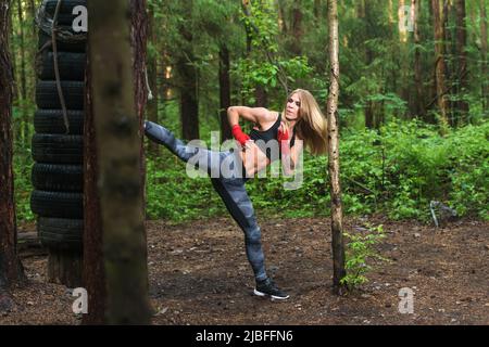 Fit girl beat high leg side kick working out outdoors. Woman fighter exercising, doing kickboxing training martial arts. Stock Photo