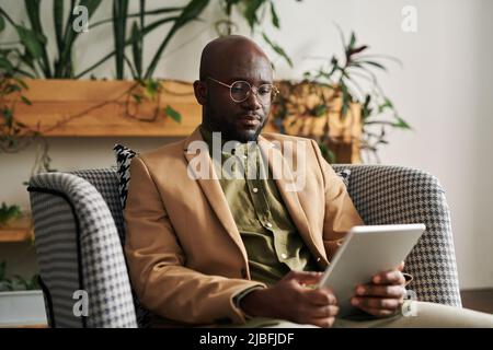 Young confident professional psychologist in formalwear having online session with patient while sitting in armchair in his office Stock Photo