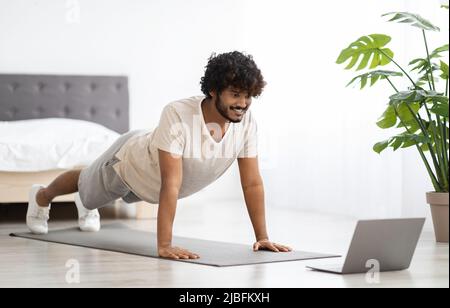 Sporty indian man planking at home, watching fitness video Stock Photo