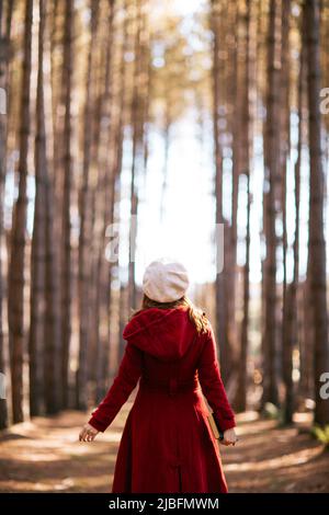 Back view of unrecognizable redhead female with outerwear and beret hat standing holding book in woods in fall Stock Photo