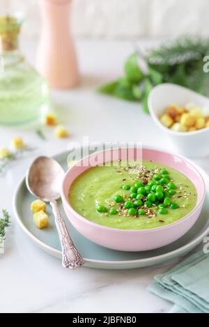 Delicious healthy cream pea soup in a bowl garnished with green peas and croutons on table Stock Photo
