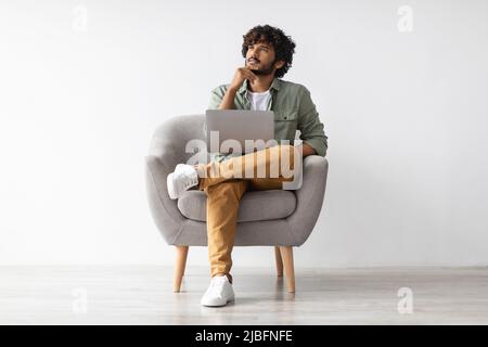 Thoughtful eastern man using computer, looking at copy space Stock Photo