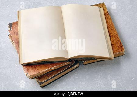 A shabby vintage book with blank pages on a stack of books on a white concrete table. Opened notepad with blank pages with copy space Stock Photo