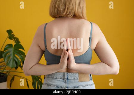 Back view of crop unrecognizable female in bra and jeans performing Paschim Namaskarasana pose while practicing yoga in bright yellow studio Stock Photo