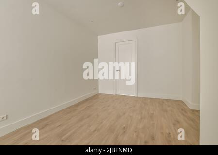 Red rose petals on white bed against blurred wineglasses and bottle of drink on table in light hotel room prepared for celebrating Saint Valentine Day Stock Photo