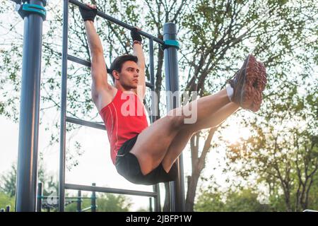 Fitnes man hanging on wall bars performing legs raises. Core cross training working out abs muscles. Stock Photo