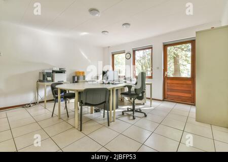 Chairs at oval table with modern computers in spacious office with whiteboard hanging on wall and tiled floor on sunny day Stock Photo