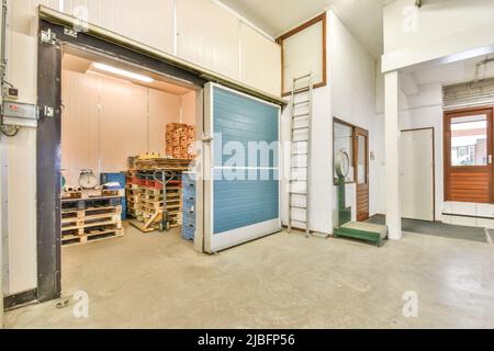 Various wooden pallets and large scales in spacious illuminated warehouse with doors and glowing lamps Stock Photo