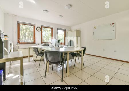 Chairs at oval table with modern computers in spacious office with whiteboard hanging on wall and tiled floor on sunny day Stock Photo