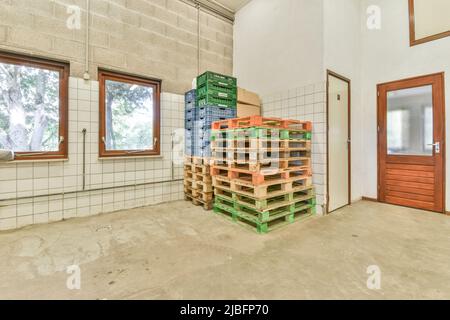 Stack of green and orange wooden pallets with plastic containers and carton boxes placed on each other in spacious storage Stock Photo
