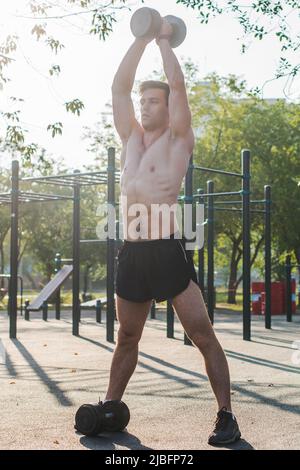 Muscular male athlete with arms raised doing lifting exercises with dumbbells Stock Photo