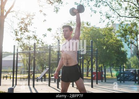 Muscular male athlete with arms raised doing lifting exercises with dumbbells Stock Photo