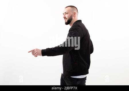 Cheerful smiling cheerful bearded man with mustache, wearing casual black outfit. Standing pointing index by forefinger Stock Photo