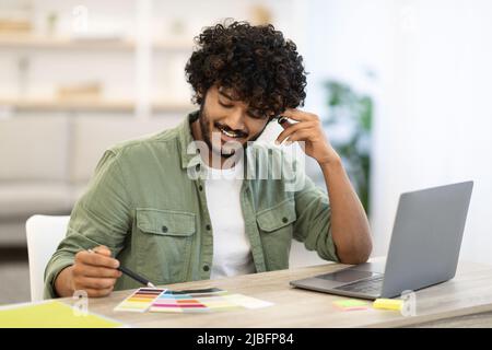 Positive hindu man web designer working on laptop, office interior Stock Photo