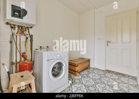 Electric water heater hanging on wall over washing machine near wooden bench in spacious laundry room with azulejo tiled floor Stock Photo