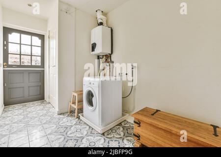 Electric water heater hanging on wall over washing machine near wooden bench in spacious laundry room with azulejo tiled floor Stock Photo
